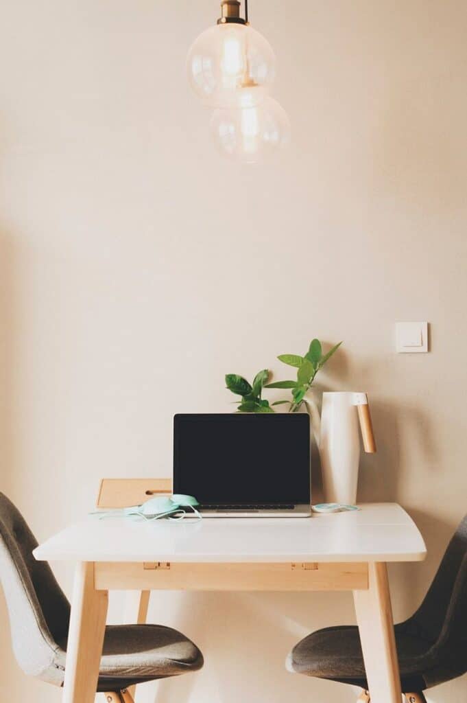 Minimal home office workspace with laptop, desk, chairs, and hanging light